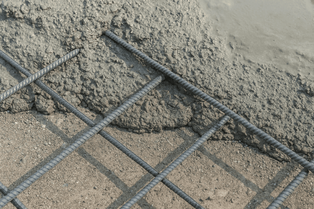 Select Strong Concrete Mix Close-up view of fresh concrete being poured over a steel rebar grid, showing the rough wet mix and reinforcement rods for strength and durability.
