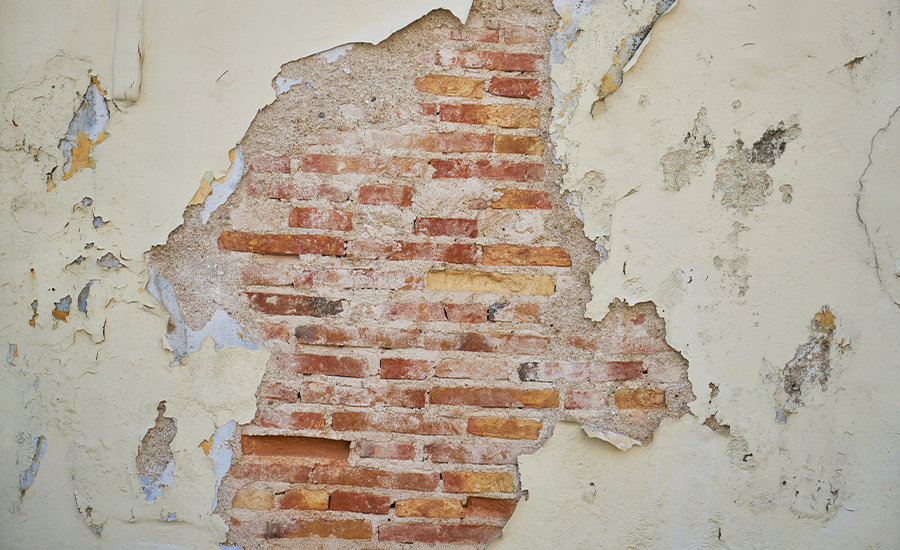 Exposed brick wall with worn struck pointing behind peeling plaster, showing masonry decay and restoration needs