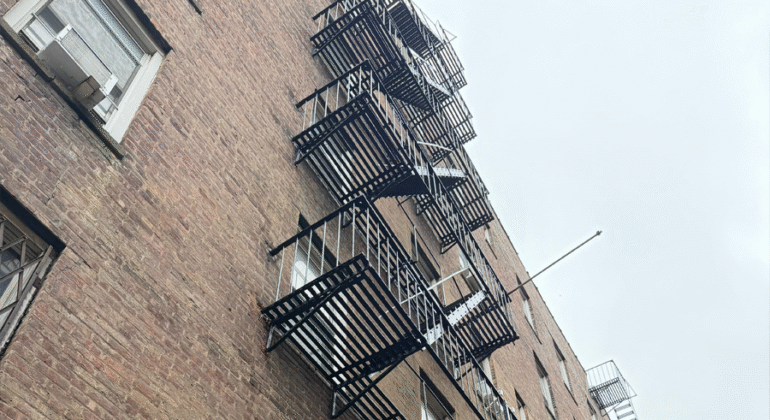 External fire escape staircase attached to a historic NYC building, showing classic iron structure and safety design under city fire code compliance.