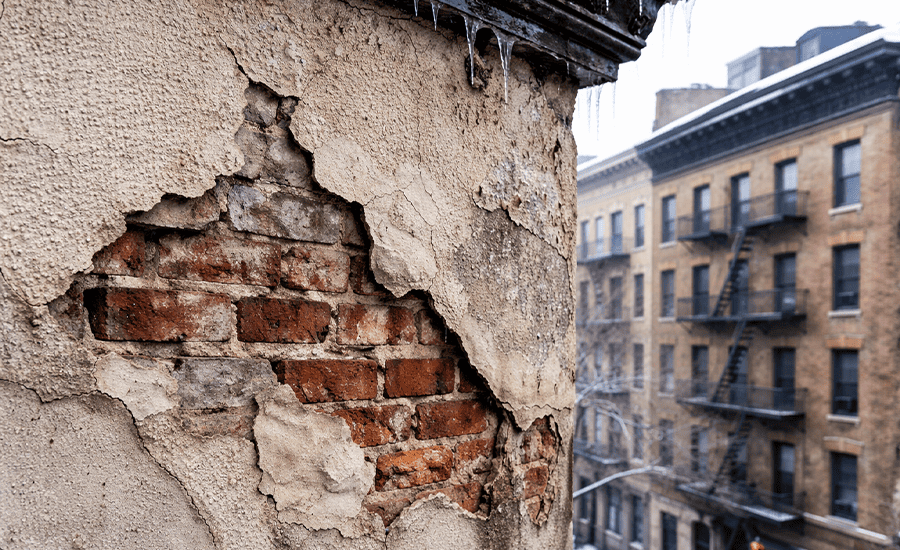 Hidden stucco damage exposing brick wall after winter freeze and thaw in NYC building