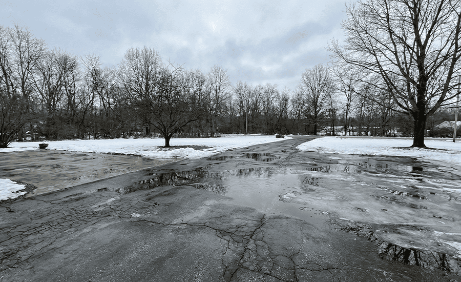 Water pooling on a cracked driveway after pressure washing in winter, showing ice formation and freeze-thaw damage risks