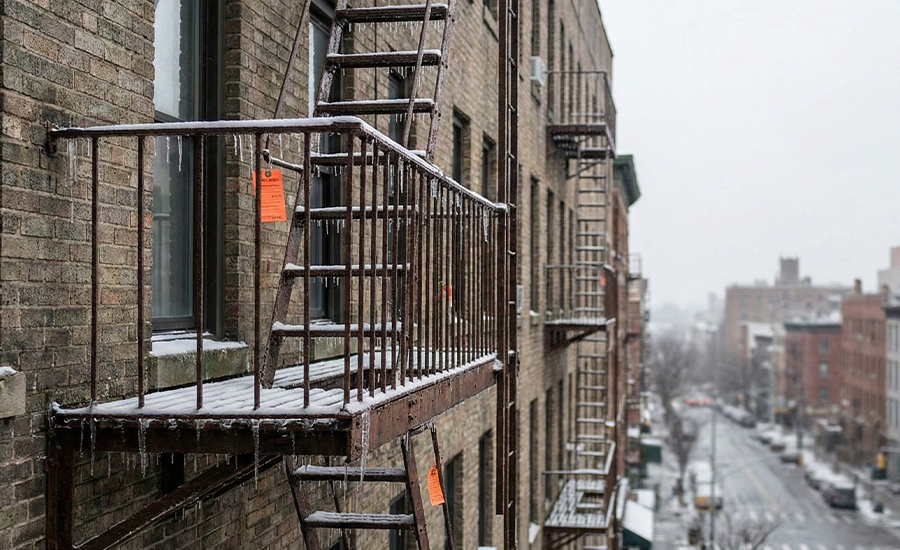 Rusty NYC fire escape covered in snow and icicles during winter, showing corrosion risks and safety concerns for landlords and residents.