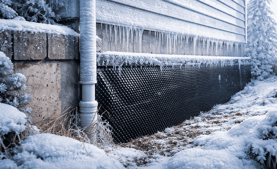 Cold weather waterproofing on building foundation with protective membrane exposed to snow and ice buildup