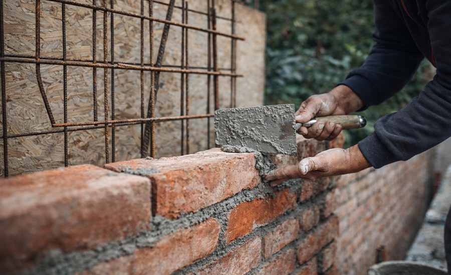 masonry contractor laying bricks with mortar during brick wall construction