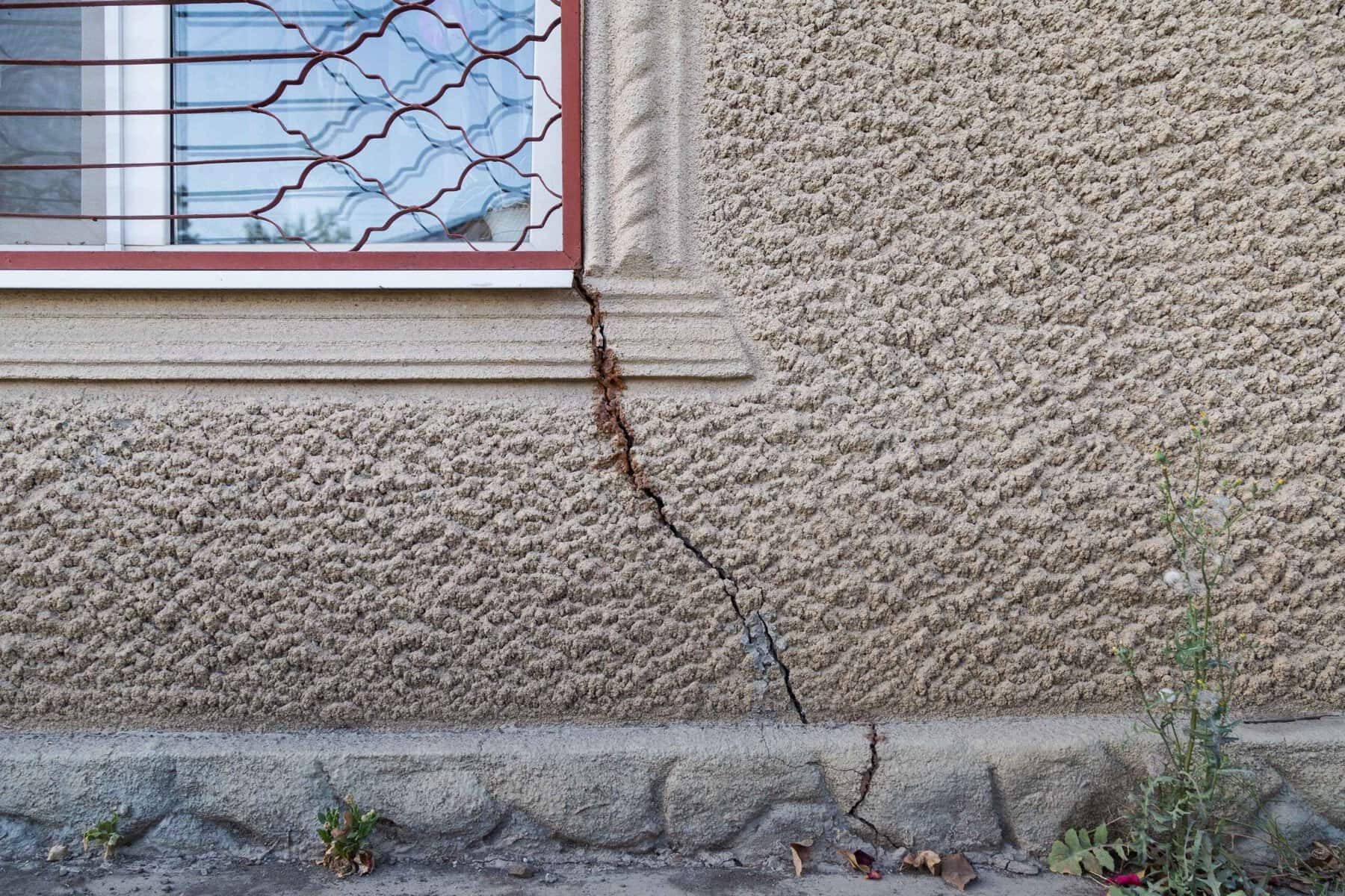 Cracked stucco wall near window showing damage caused by moisture and structural movement in NYC building