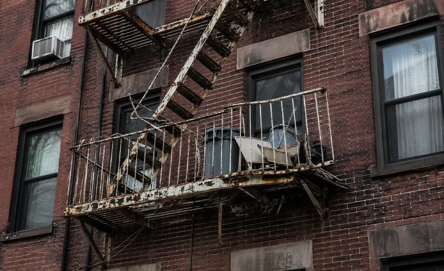 Non-compliant NYC fire escape with rust and blocked access concerns